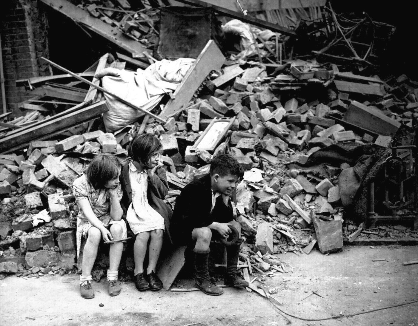 Bambini seduti davanti alle macerie della loro casa